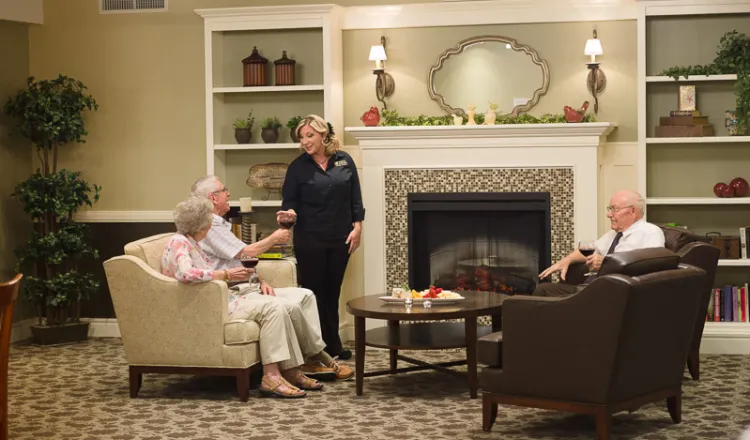 Two men and one woman seated near a fire place being served glasses of wine