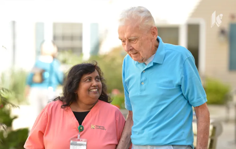 A nurse and a senior walk together outside in a courtyard