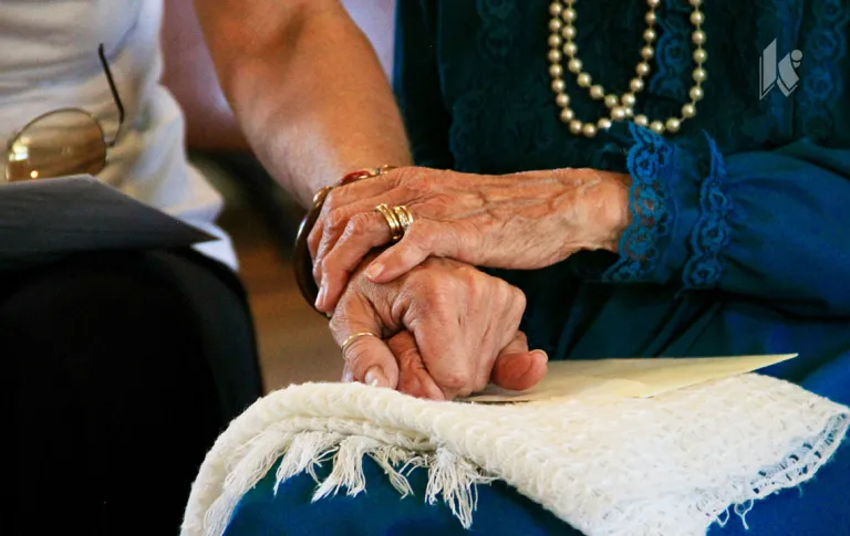 Two elderly hands clasped on a lap