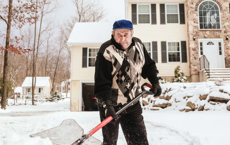 An elderly man is seen shoveling snow in front of a house.