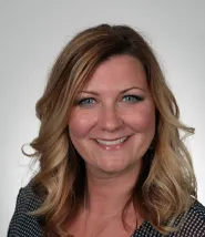 Headshot of Adrienne Bailey, she is wearing a black and white polka dot shirt and has medium length blonde hair in loose curls. 