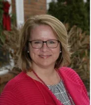 Sharon's headshot, she is wearing a magenta cardigan with a black and white striped shirt below. 